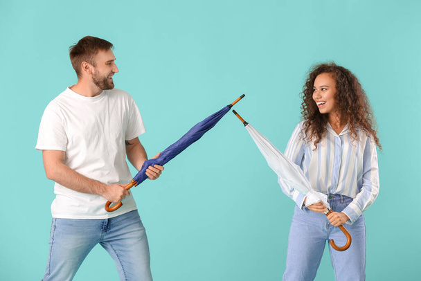 Glückliches junges Paar mit Regenschirmen auf farbigem Hintergrund - Foto, Bild