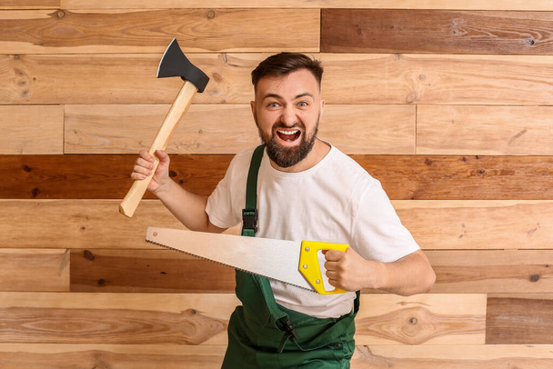 Handsome lumberjack with axe and saw on wooden background - Photo, Image