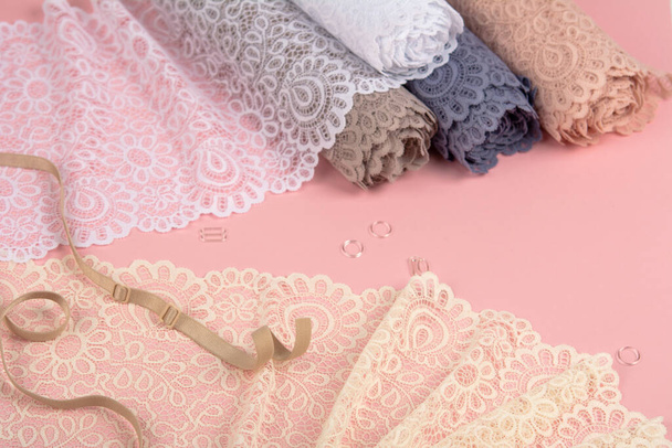 Roll of Delicate color laces for panties and bras on pink background with plastic fittings. Elastic material. Using for Atelier and fabric store. - Fotó, kép