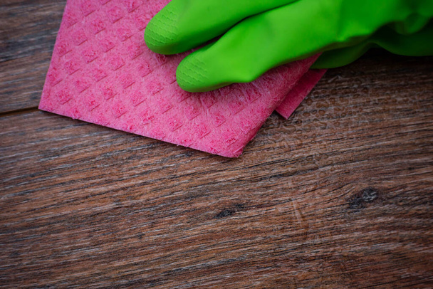 Closeup of a hand in a green rubber glove rubbing a wet wooden surface. The concept of disinfection of premises, the prevention of viral and bacterial diseases. Cleaning wooden surfaces. - Photo, image