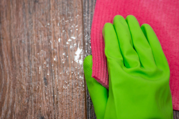 Closeup of a hand in a green rubber glove rubbing a wet wooden surface. The concept of disinfection of premises, the prevention of viral and bacterial diseases. Cleaning wooden surfaces. - Φωτογραφία, εικόνα