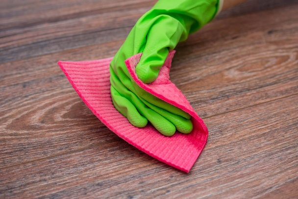 Closeup of a hand in a green rubber glove rubbing a wet wooden surface. The concept of disinfection of premises, the prevention of viral and bacterial diseases. Cleaning wooden surfaces. - Фото, изображение