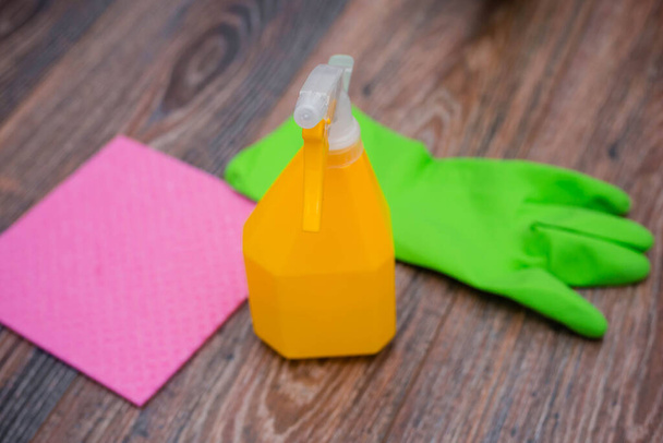 Close-up of a spray bottle, rubber gloves and a wet rag lying on the floor. The concept of disinfection of premises, the prevention of viral and bacterial diseases. Cleaning wooden surfaces. - Фото, изображение