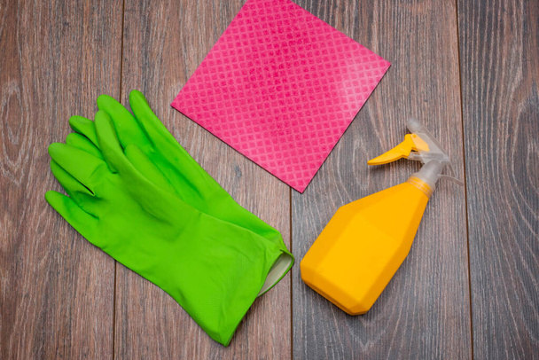 Close-up of a spray bottle, rubber gloves and a wet rag lying on the floor. The concept of disinfection of premises, the prevention of viral and bacterial diseases. Cleaning wooden surfaces. - Photo, image