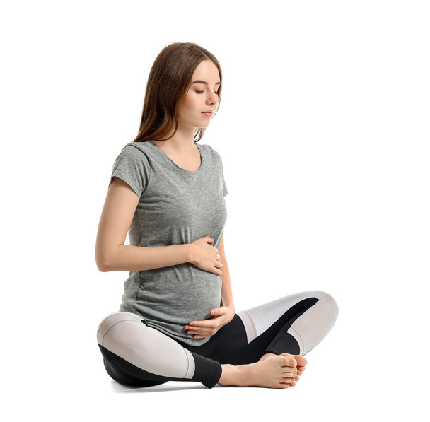 Νεαρή έγκυος γυναίκα που ασκεί γιόγκα σε λευκό φόντο - Φωτογραφία, εικόνα