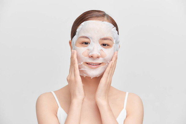 Heureuse jeune femme asiatique en utilisant un masque cosmétique isolé sur fond blanc. - Photo, image