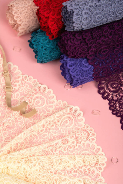 Roll of Delicate color laces for panties and bras on pink background with plastic fittings. Elastic material. Using for Atelier and fabric store. - 写真・画像