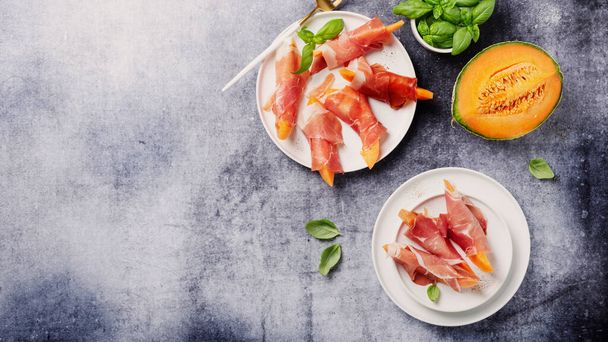 Summer appetizer with sweet melon and ham on dark background. Top view image with copy space, slider format - Fotó, kép