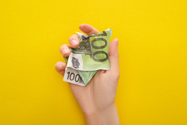 oříznutý pohled na ženu držící zmačkanou eurobankovku izolovanou na žluté - Fotografie, Obrázek