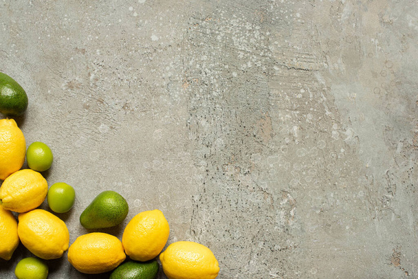 top view of colorful limes, avocado and lemons on grey concrete surface - Foto, Imagen