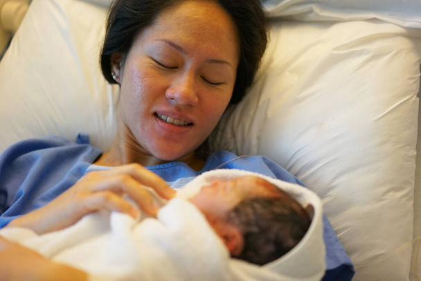 Asian Chinese woman smiling and holding her new born baby right after childbirth - Photo, Image