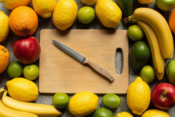 top view of tasty colorful fruits and wooden cutting board with knife - Foto, afbeelding