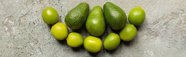 top view of green avocado, limes on grey concrete surface, panoramic shot - Zdjęcie, obraz