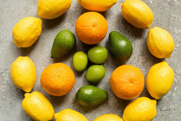 top view of colorful oranges, avocado, limes and lemons arranged in circle on grey concrete surface - Foto, afbeelding