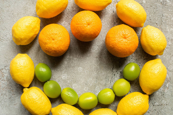 top view of colorful oranges, avocado, limes and lemons arranged in circle on grey concrete surface - Foto, Imagem