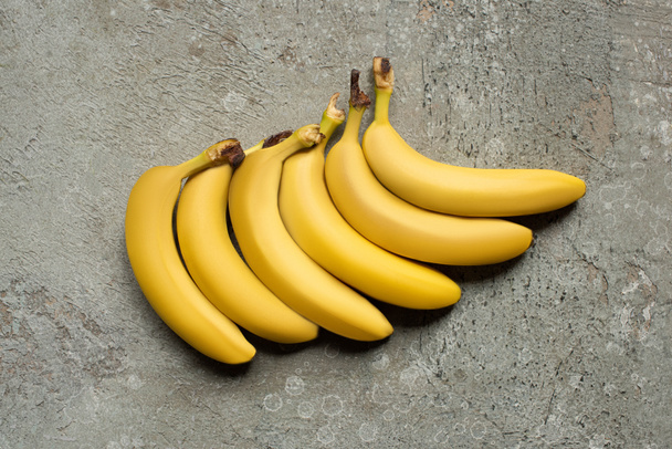 top view of colorful delicious bananas on grey concrete surface - Foto, Imagem