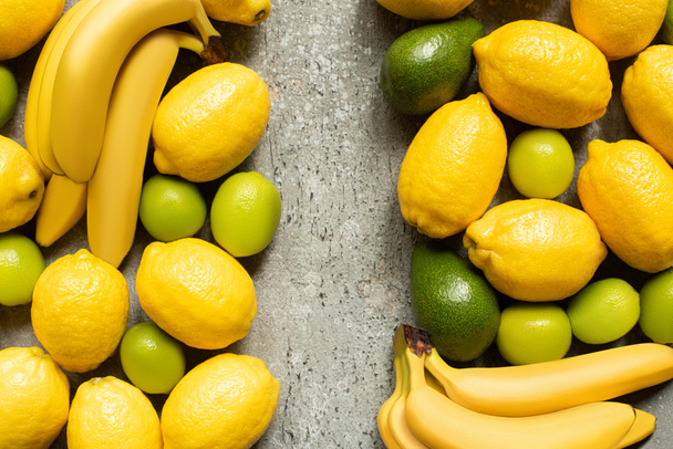 top view of colorful bananas, avocado, limes and lemons on grey concrete surface - Photo, Image