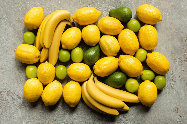 top view of colorful bananas, avocado, limes and lemons on grey concrete surface - Photo, image