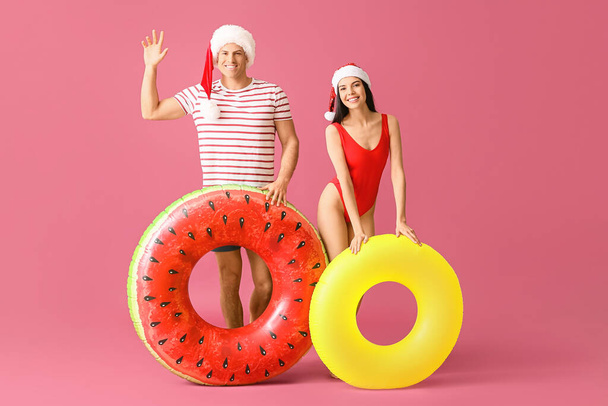 Young couple with inflatable rings and Santa hats on color background - Photo, Image