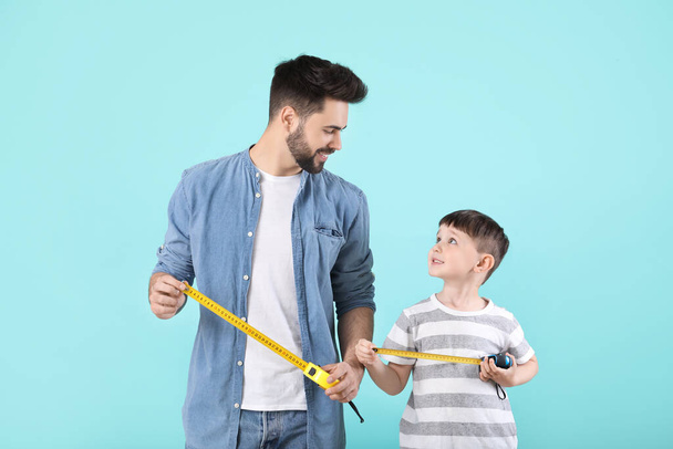 Father and son with measuring tapes on color background - Photo, Image