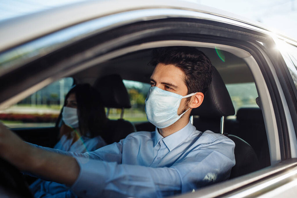 Junger Mann Taxifahrer trägt sterile medizinische Maske im Auto. Ein Junge am Steuer des Autos, der sicher aus geschäftlichen Gründen unterwegs ist und soziale Distanz hält. Coronavirus-Pandemiekonzept - Foto, Bild