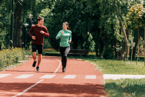 Couple souriant tout en faisant du jogging sur la piste de course dans le parc  - Photo, image