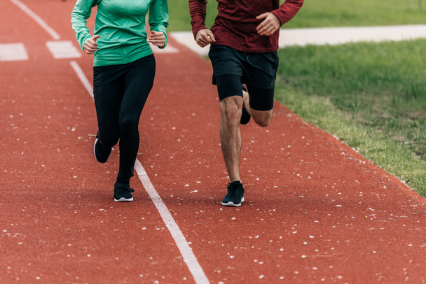 Cropped view of couple jogging together on running track in park  - Фото, зображення