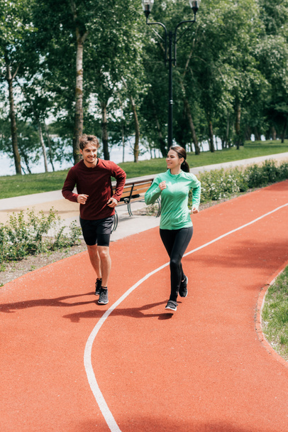 mooie vrouw glimlachen terwijl joggen in de buurt vriendje op running track in park  - Foto, afbeelding