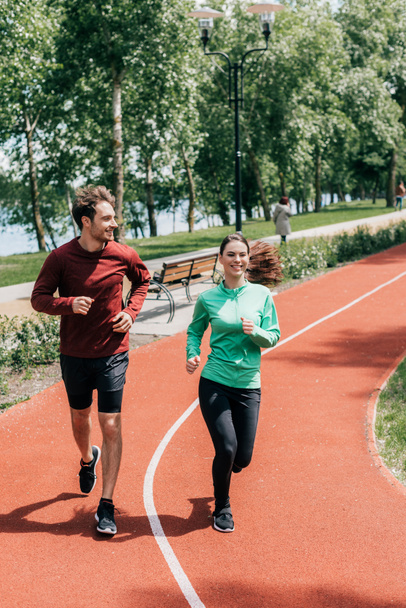 Handsome man smiling near girlfriend during jogging in park  - Photo, Image