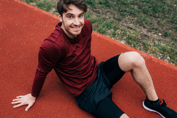 High angle view of handsome runner smiling at camera on running track in park  - Foto, immagini