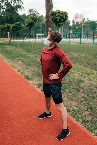 Спортсмен в медичній масці з руками на тренуваннях стегон в парку
  - Фото, зображення