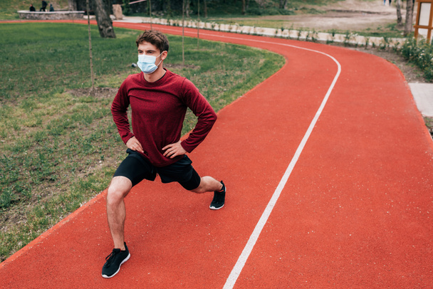 Esportista em máscara médica fazendo lunges enquanto trabalhava no caminho de corrida no parque
  - Foto, Imagem