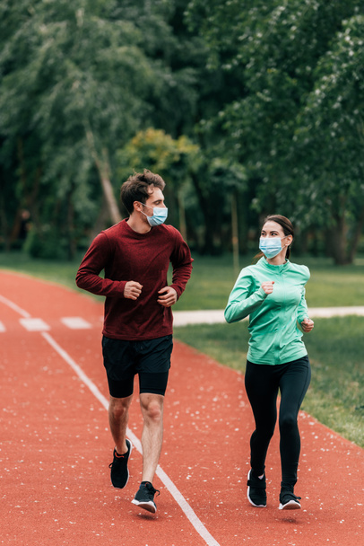 Couple in medical masks jogging together on running path in park  - Photo, Image