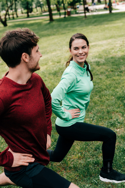 Selective focus of beautiful woman smiling at man while doing lunges in park  - Foto, imagen