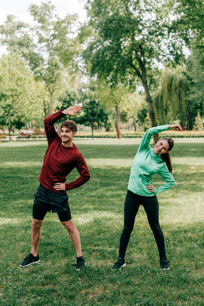 Giovane coppia sorridente che si allena sul prato erboso nel parco
  - Foto, immagini