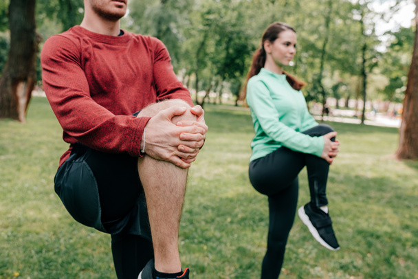 A pár nyújtózkodó lábainak szelektív fókusza a parkban való edzés közben  - Fotó, kép