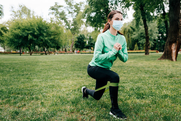 Young sportswoman in medical mask training with resistance band in park  - Φωτογραφία, εικόνα