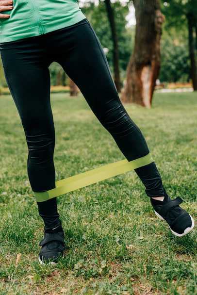 Cropped view of sportswoman using resistance band while training in park  - Fotografie, Obrázek