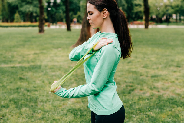 Side view of beautiful sportswoman pulling up resistance band in park  - Foto, Imagem