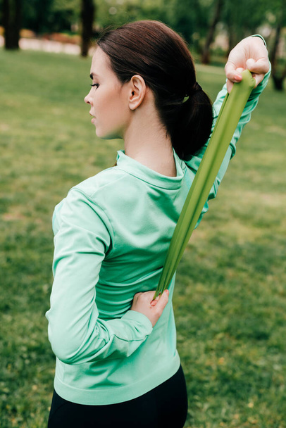 Pohled zezadu na mladou sportovkyni používající odbojovou pásku při cvičení v parku  - Fotografie, Obrázek
