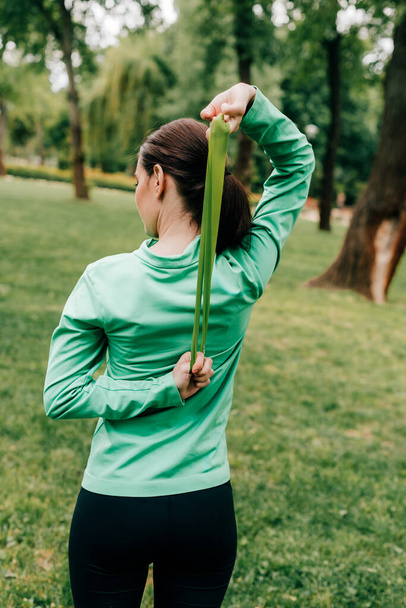 Back view of sportswoman exercising with resistance band in park  - Photo, Image