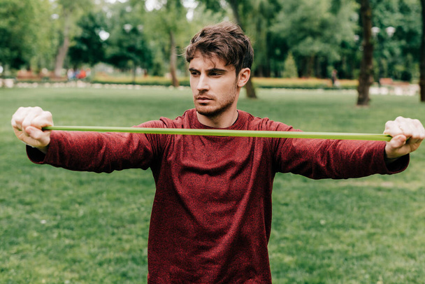Красивый спортсмен подтягивает эластичный браслет в парке
  - Фото, изображение