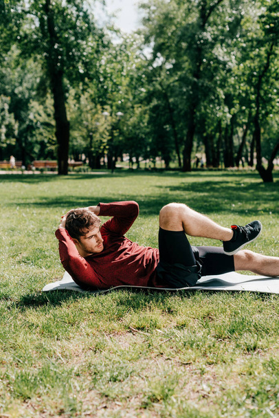 Вид сбоку на человека, делающего абс во время тренировки на фитнес-коврике в парке
  - Фото, изображение