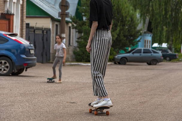Young girl in a black T-shirt and striped trousers learns to ride a skateboard - Foto, imagen