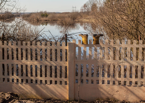 Bottes en caoutchouc jaune sur la clôture sur le fond d'une rivière débordante - Photo, image