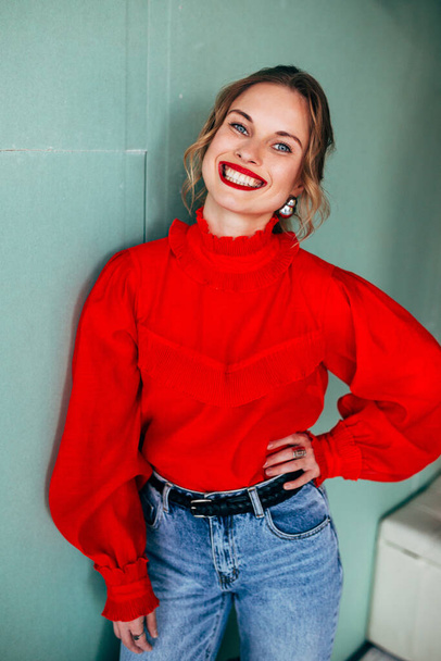 Cheerful blonde in red sweater on green background - Valokuva, kuva