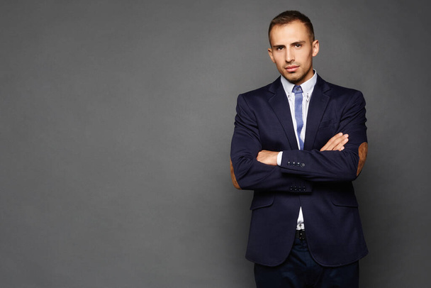 Confident businessman in suit isolated at dark background. A handsome young man in an official outfit standing with crossed arms. - Foto, immagini