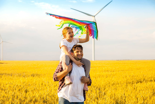 Happy father's day. Father giving her daughter a piggyback ride, having fun, playing with kite together on the Wheat Field - Photo, Image