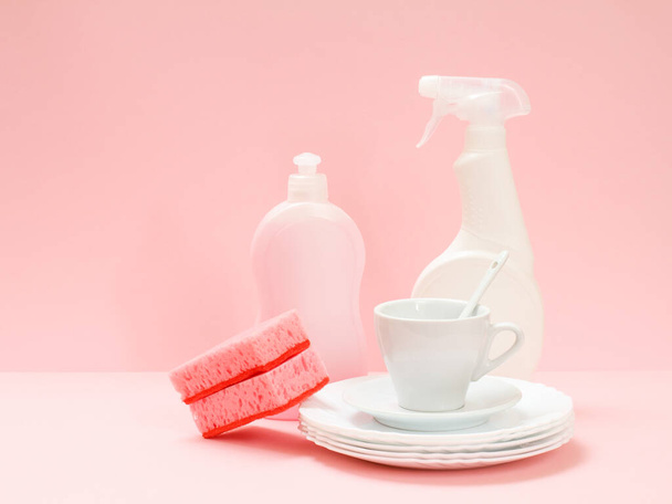 Butelki płynu do zmywania naczyń, gąbki, białe talerze, talerz i kubek na różowym tle. Koncepcja mycia i czyszczenia. - Zdjęcie, obraz