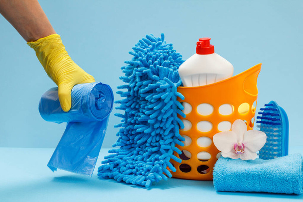 Dámská ruka v nitrilové ochranné rukavici drží pytle na odpadky s mytí a čištění sada na modrém pozadí. - Fotografie, Obrázek